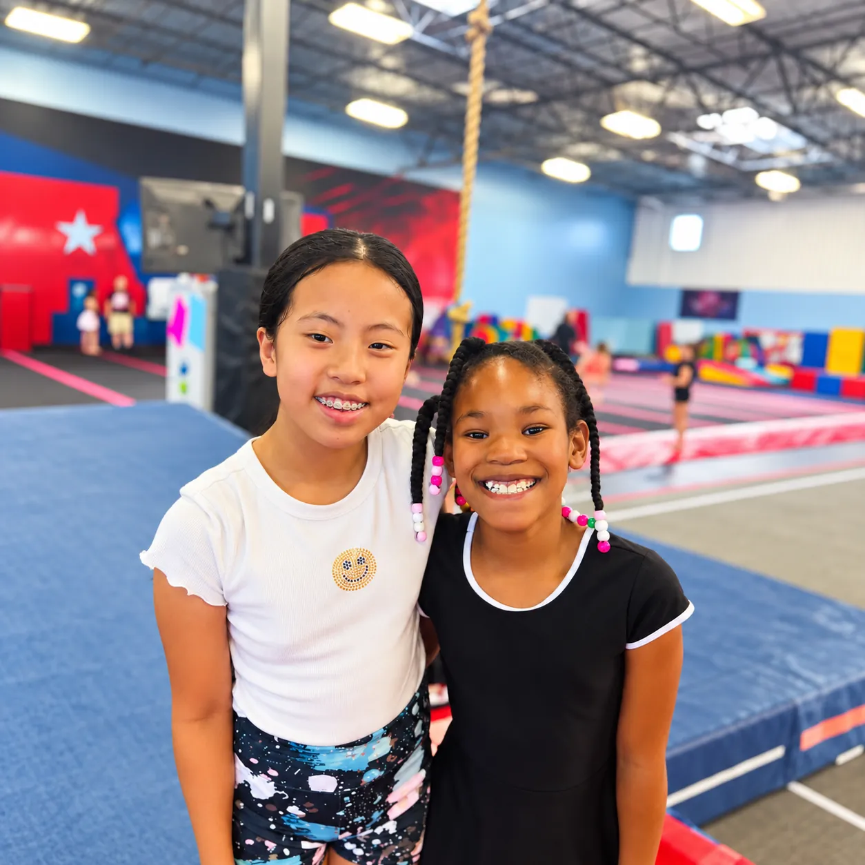 Two girls standing side by side and smiling on the gym floor