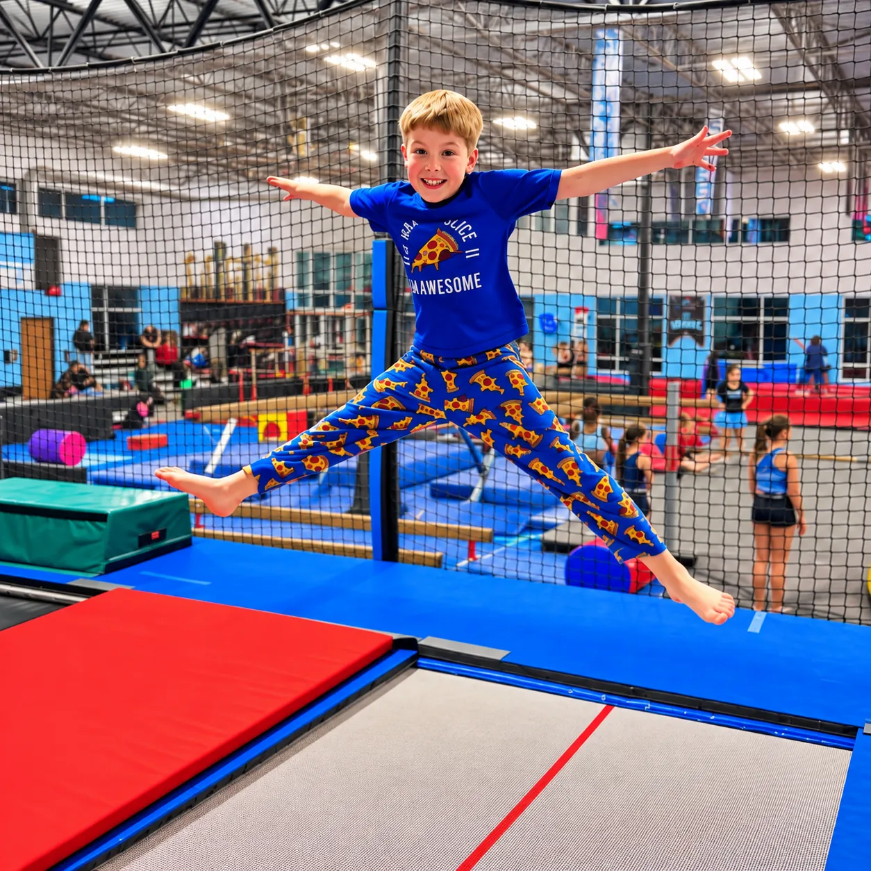 A boy in pizza-print pants doing a star jump on a trampoline